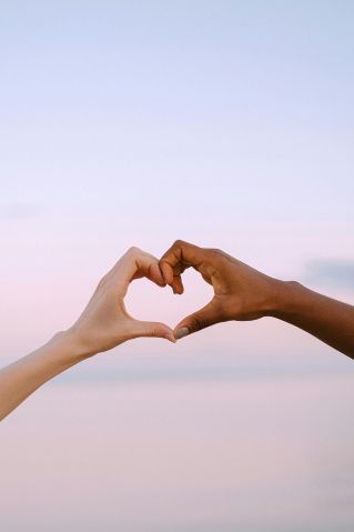 A powerful image of unity and diversity with two hands forming a heart against a serene pastel sky.